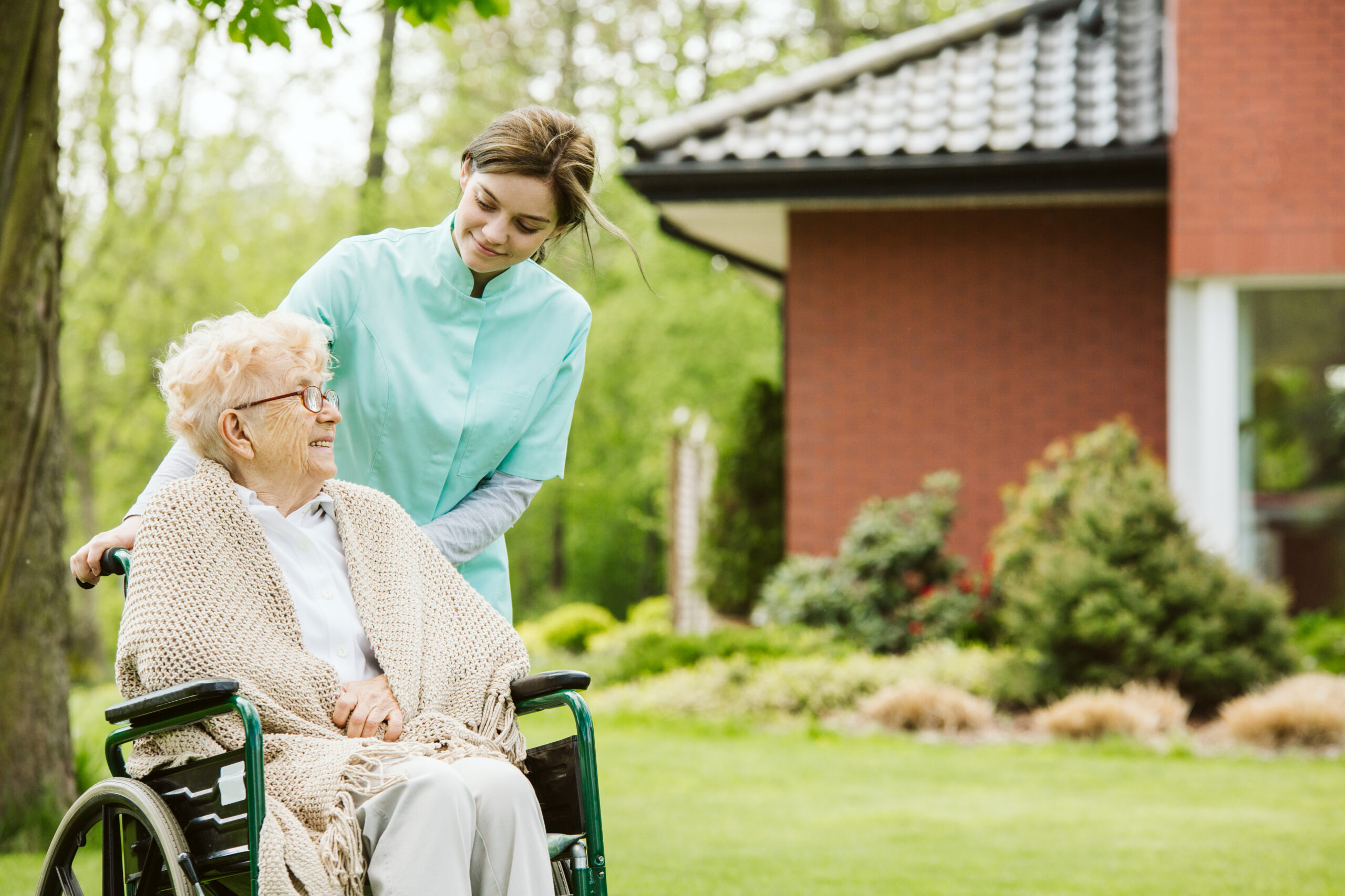 Senior disabled woman with caregiver in the garden of the nursing home