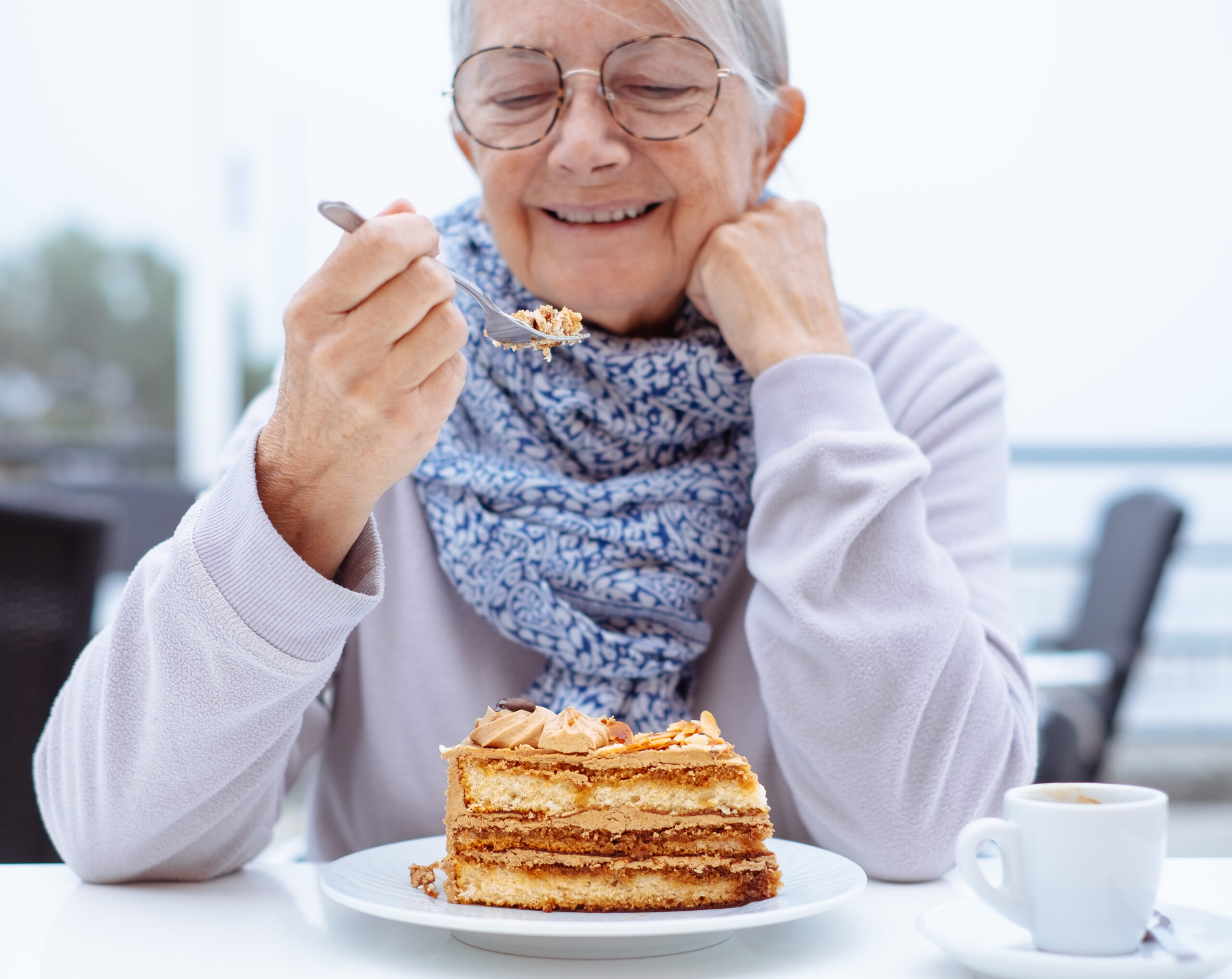 Happy senior woman sitting outdoors at cafe table with a slice o
