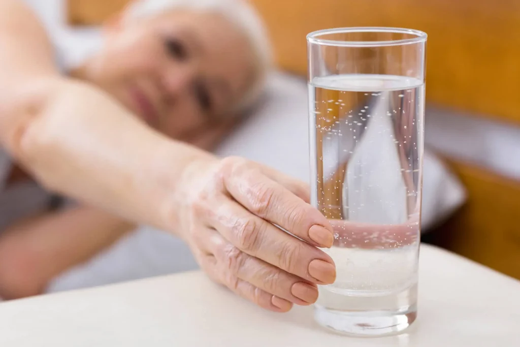 szklanka z wodą po którą sięga seniorka